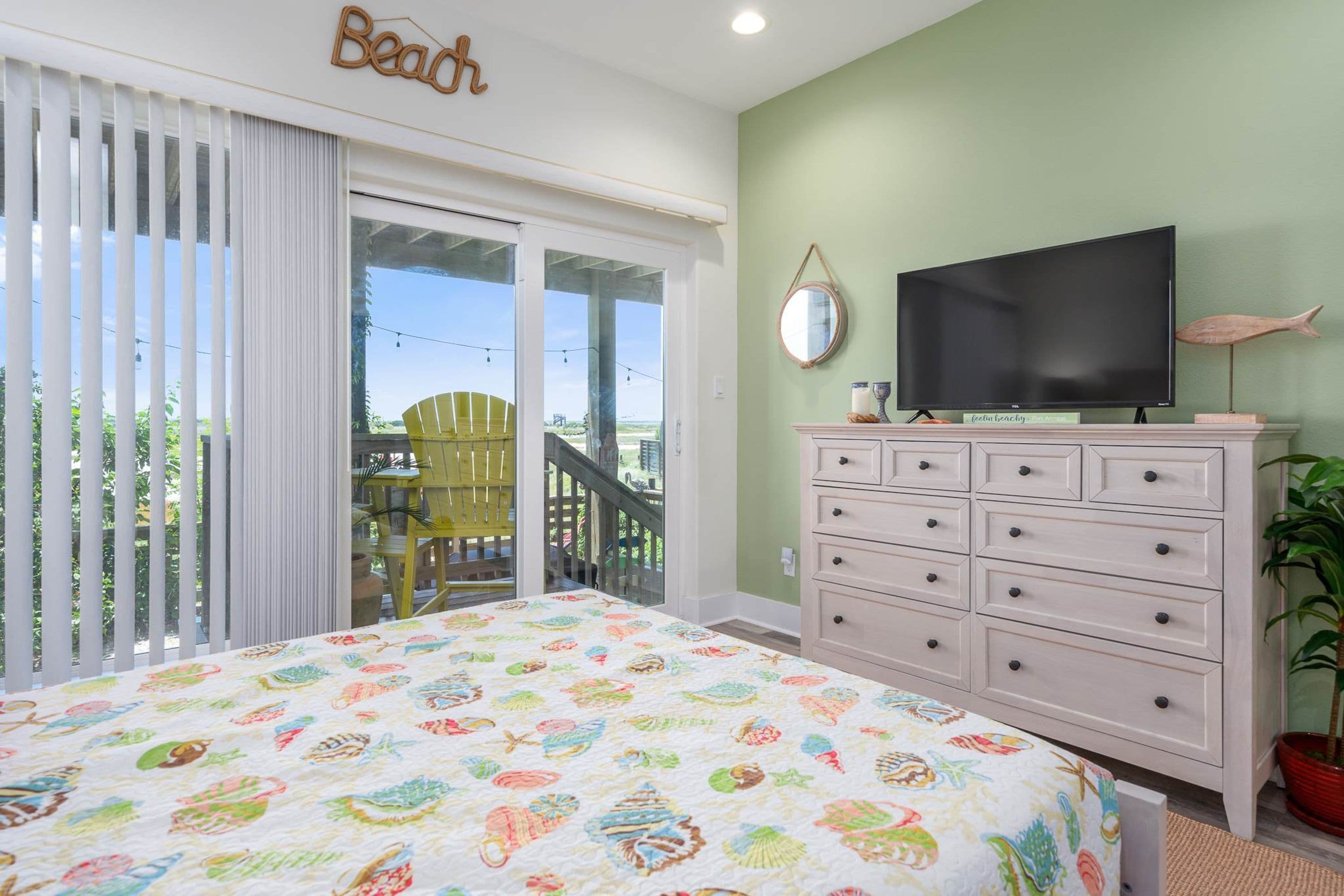 A bedroom with a bed, a television, a dresser, and a balcony with a chair.