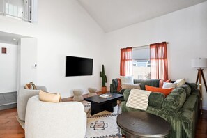 Ein modernes Wohnzimmer mit Flachbildfernseher, einem grünen Sofa, einem weißen Sessel und einem Couchtisch.