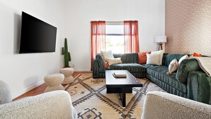 Ein Wohnzimmer mit einer Sofagarnitur, einem Couchtisch, einem Kaktus und einem an der Wand befestigten Fernseher.