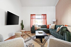 Ein Wohnzimmer mit einer Sofagarnitur, einem Couchtisch, einem Kaktus und einem an der Wand befestigten Fernseher.