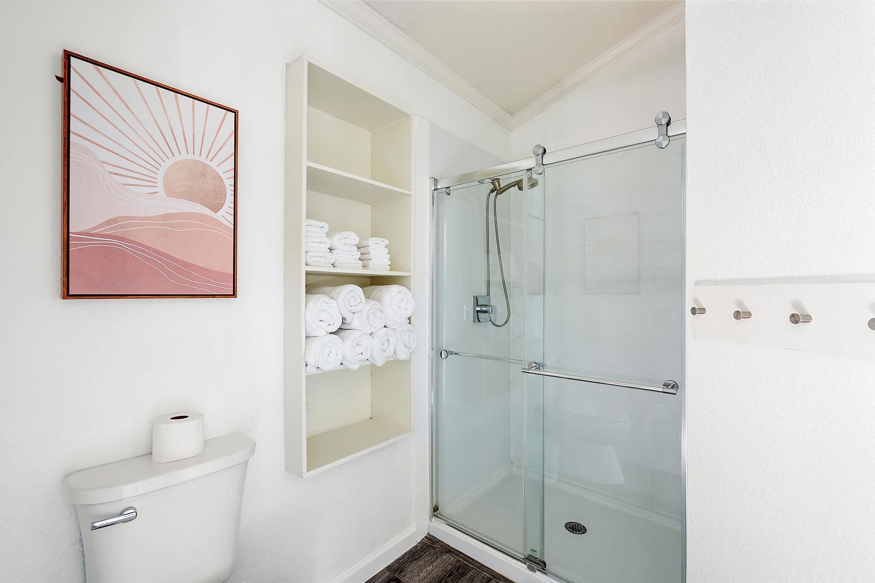 A bathroom with a glass shower enclosure, a toilet, and a shelf with neatly folded towels.