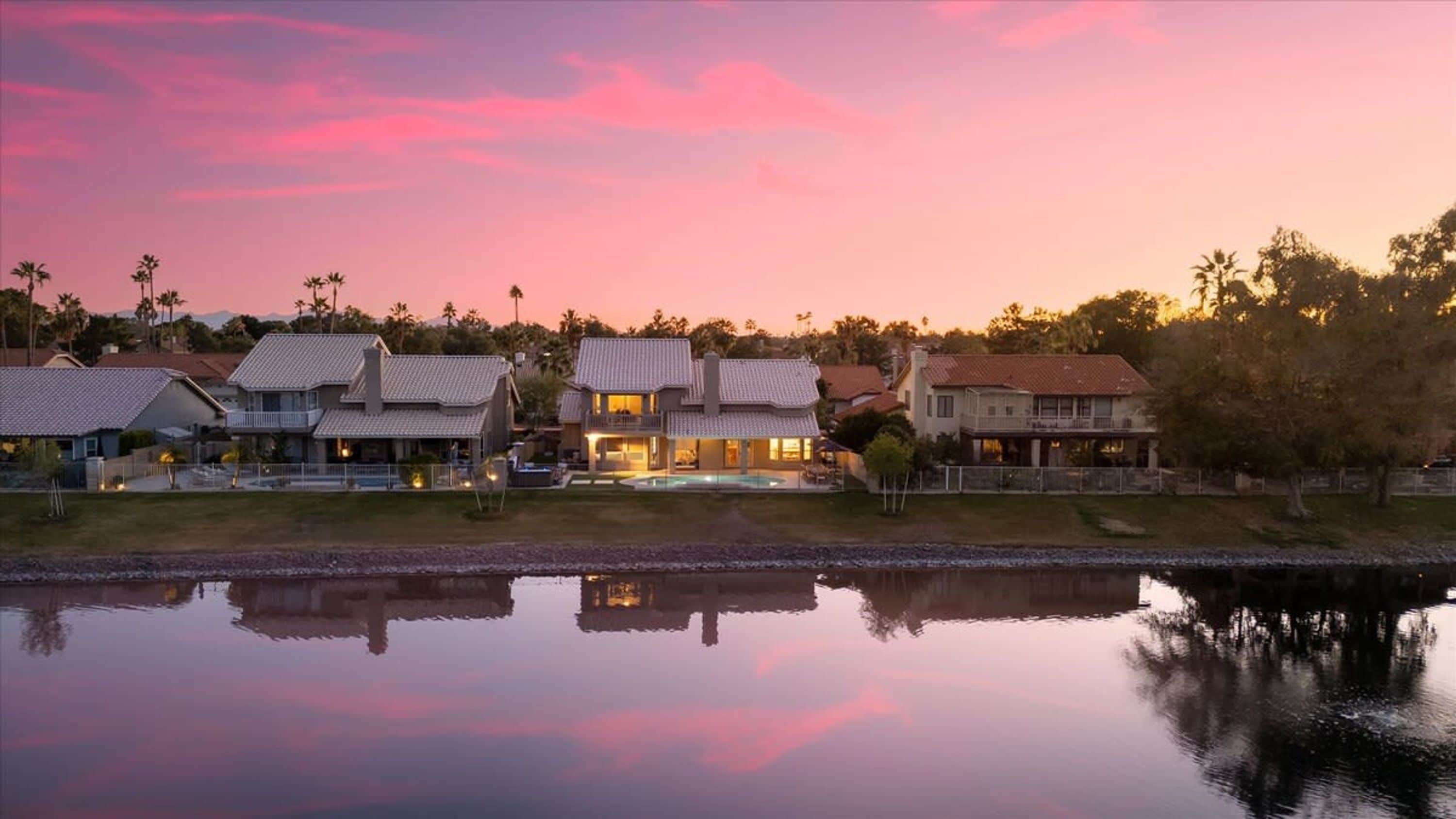 A residential area with houses, a swimming pool, and a calm body of water reflecting the buildings.