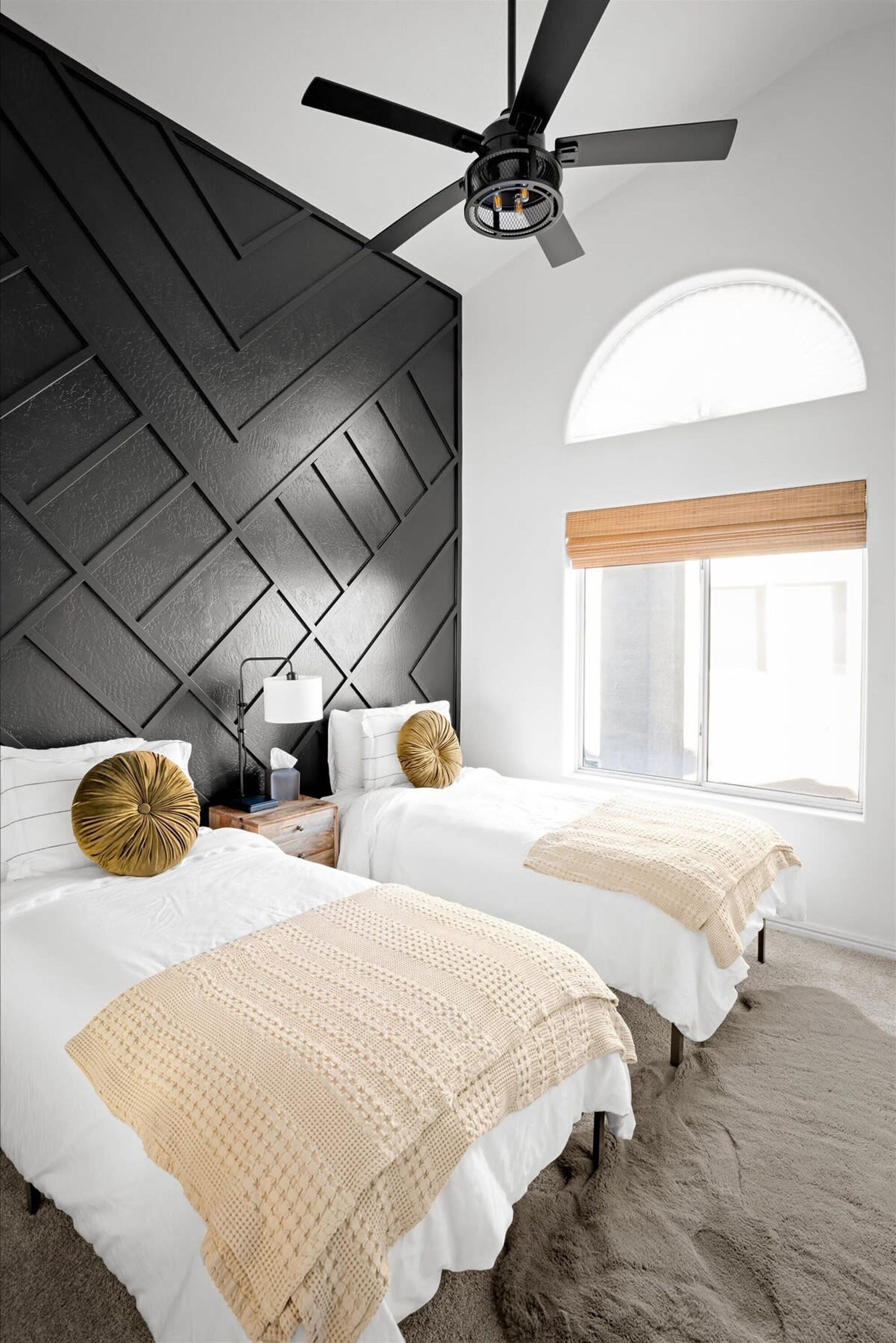 Ein Schlafzimmer mit zwei Betten, einem Deckenventilator, einem Nachttisch, einer Lampe, einem Fenster mit Ausblick und einer strukturierten Wand.