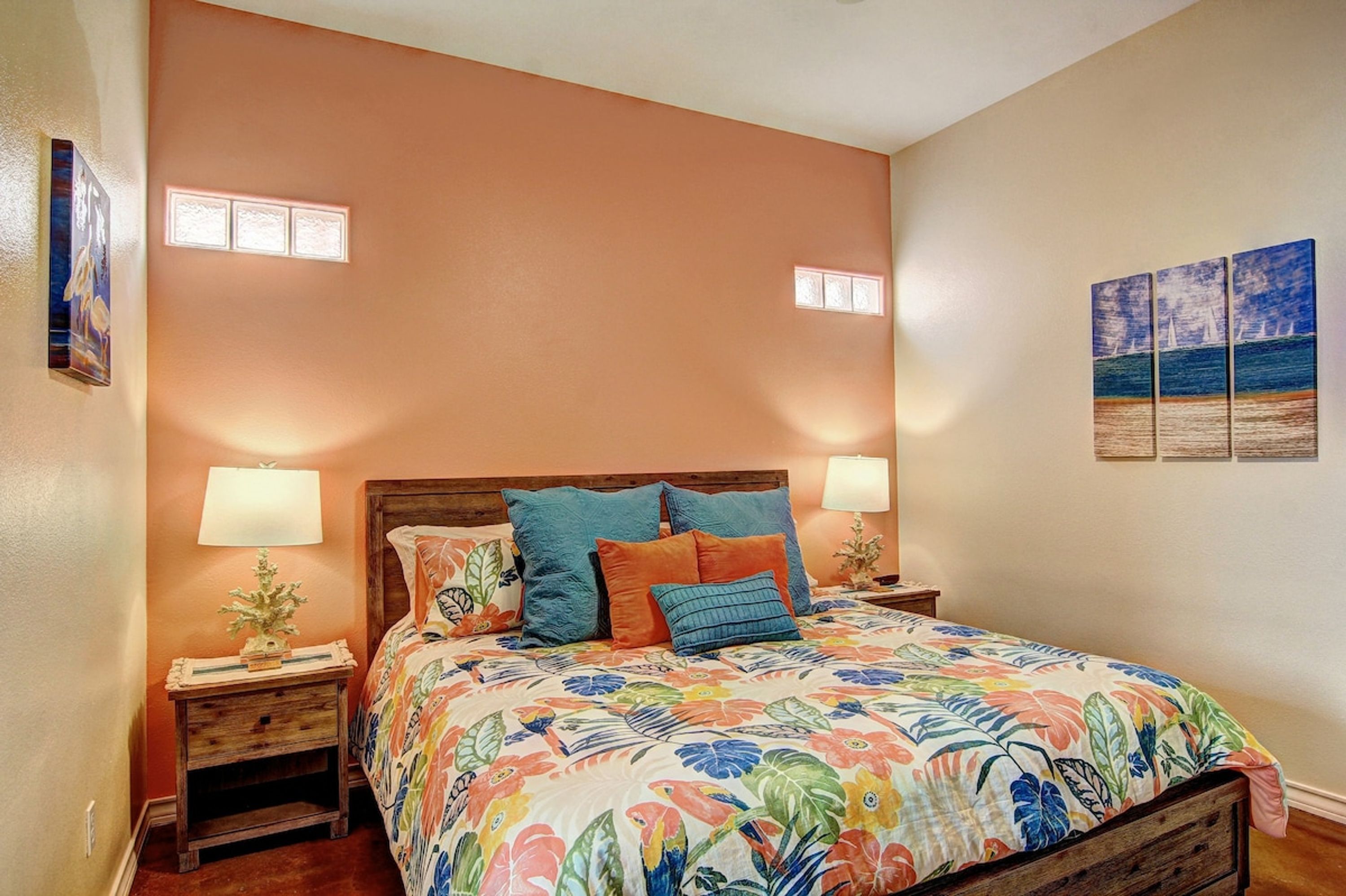 A bedroom with a floral bedspread, two bedside lamps, a wooden nightstand, and a small potted plant.