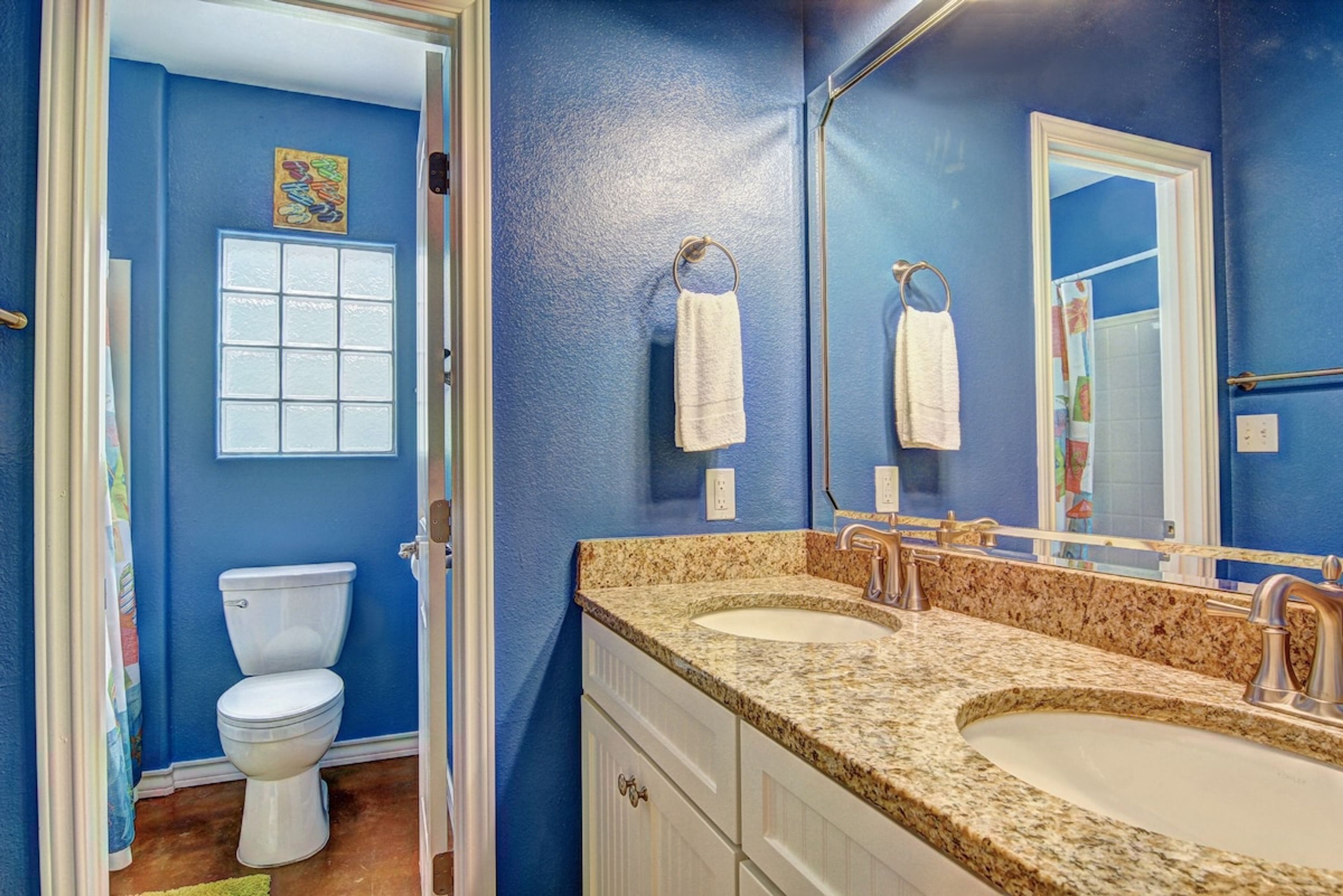 A bathroom with a toilet, two sinks, a mirror, and a towel rack.