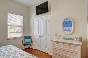 A bedroom with a bed, a chair, a dresser, a television, and a window with blinds.