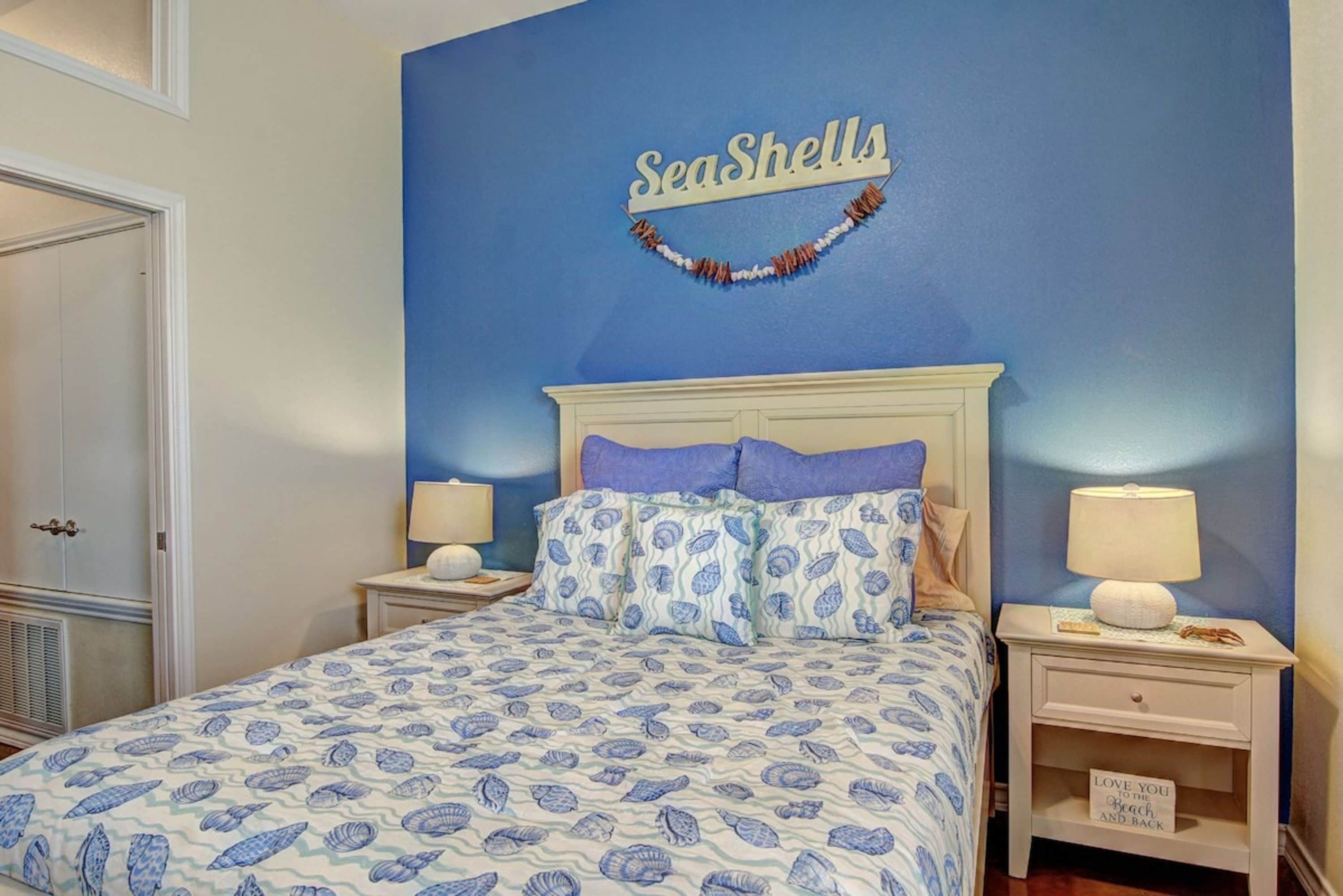 A bedroom with a bed, two bedside tables, and a wall sign that reads 'SeaShells'.