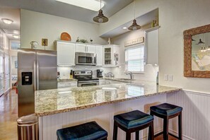 Cocina con armarios blancos, electrodomésticos de acero inoxidable, encimera de granito y una barra con taburetes.