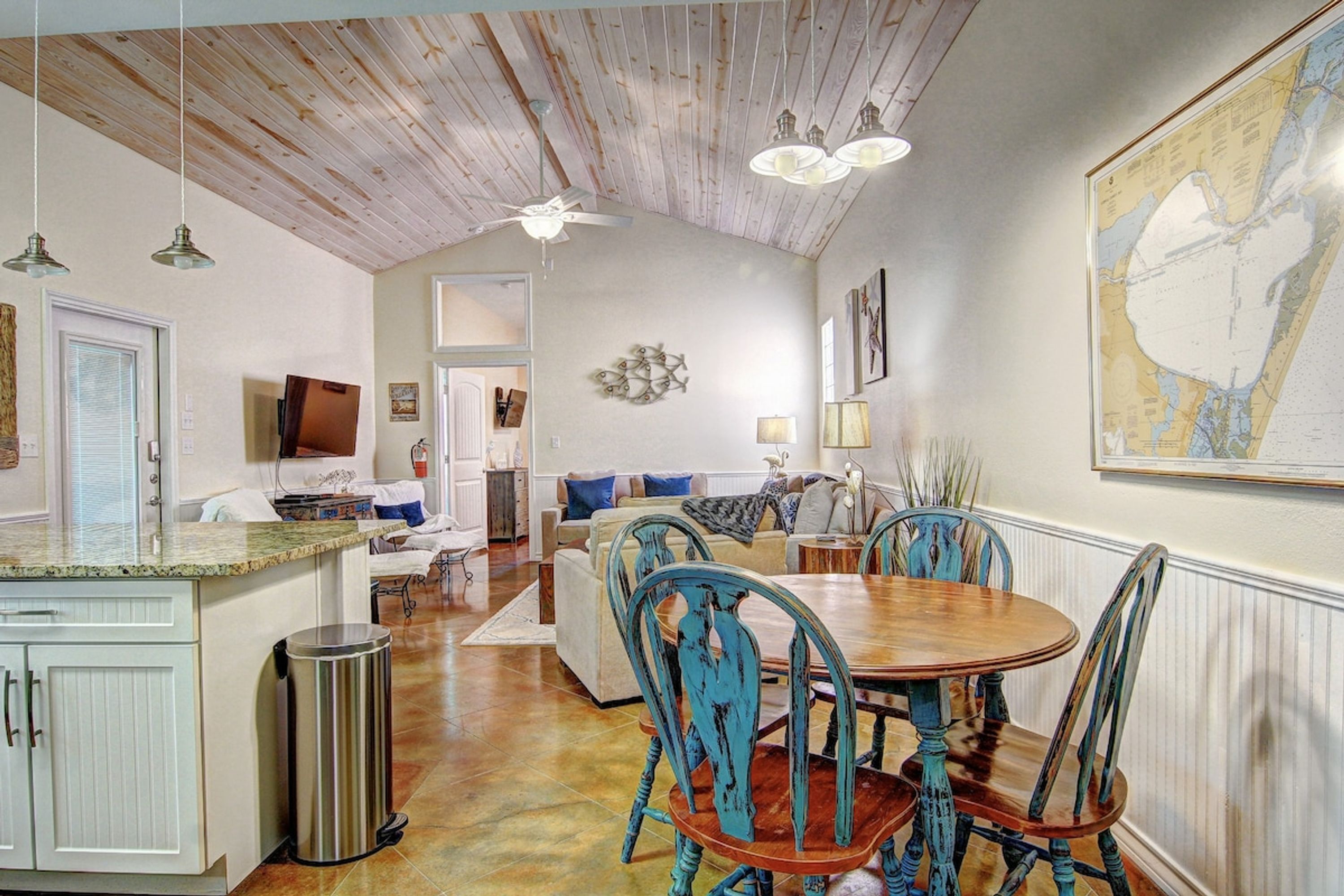 Amplia sala de estar con mesa de comedor, sillas y área de cocina con armarios y un cubo de basura.