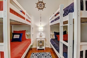 Um quarto pequeno com beliches, um leme no teto, uma mesinha com abajur e um tapete estampado.