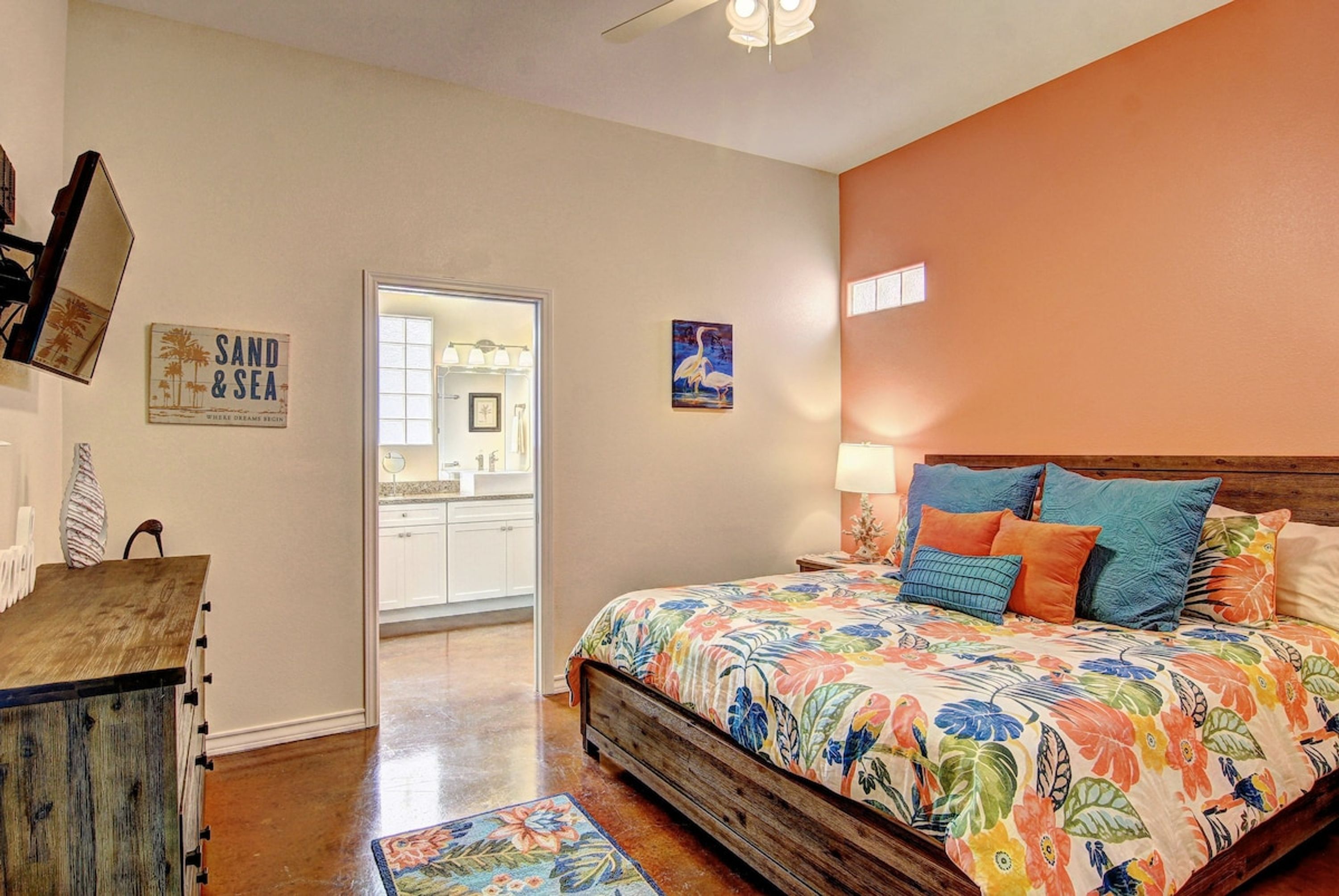 A bedroom with a wooden bed, a nightstand, a wall-mounted lamp, and a door leading to a bathroom.