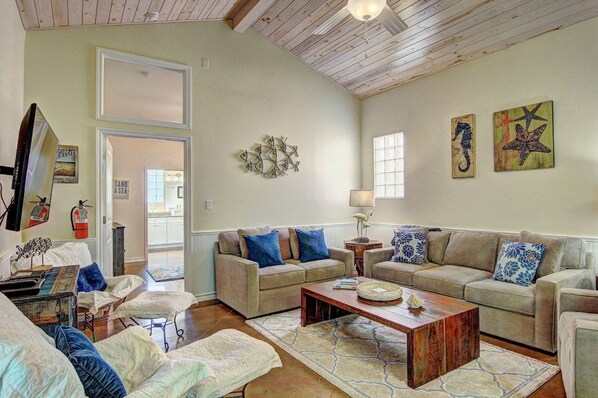 A living room with a high ceiling, a sofa set, a coffee table, and artwork on the walls.