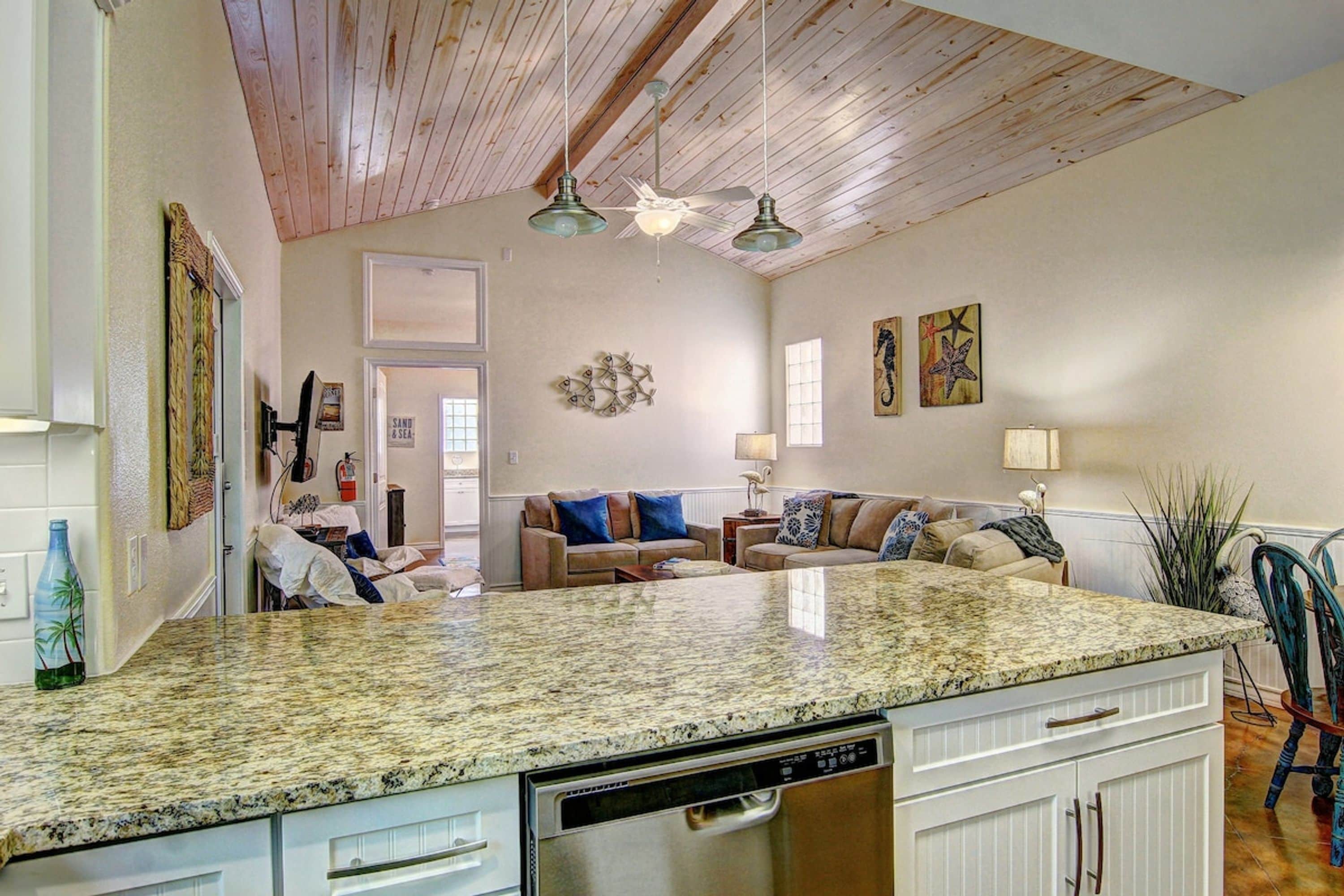 A kitchen with a granite countertop, white cabinetry, and a dishwasher.