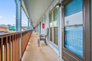 A covered balcony with a wooden railing, a chair, and a view of the surrounding buildings. - Seagull 26- Newly Renovated Close to Beach (Port Aransas)
