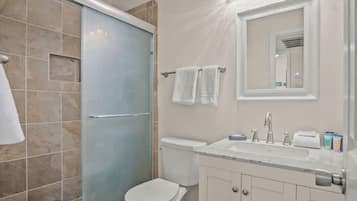 A bathroom with a shower, toilet, sink, and mirror.