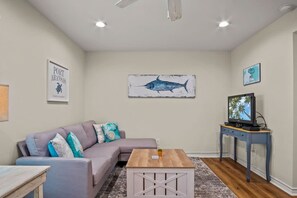 A living room with a sectional sofa, a coffee table, a television on a stand, and artwork on the walls. - Seagull 26- Newly Renovated Close to Beach (Port Aransas)