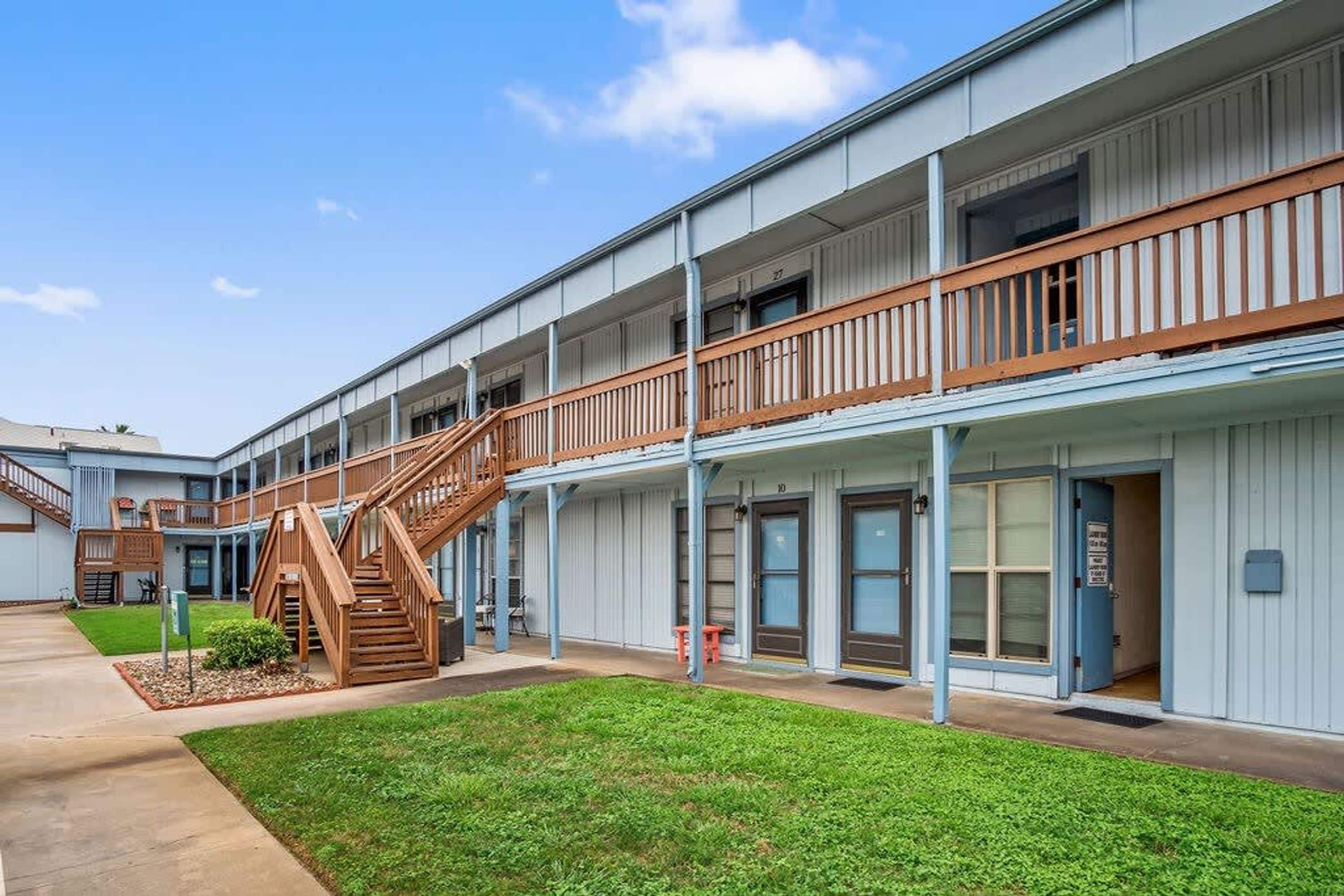 A multi-story building with a central staircase, balconies, and a well-maintained lawn.