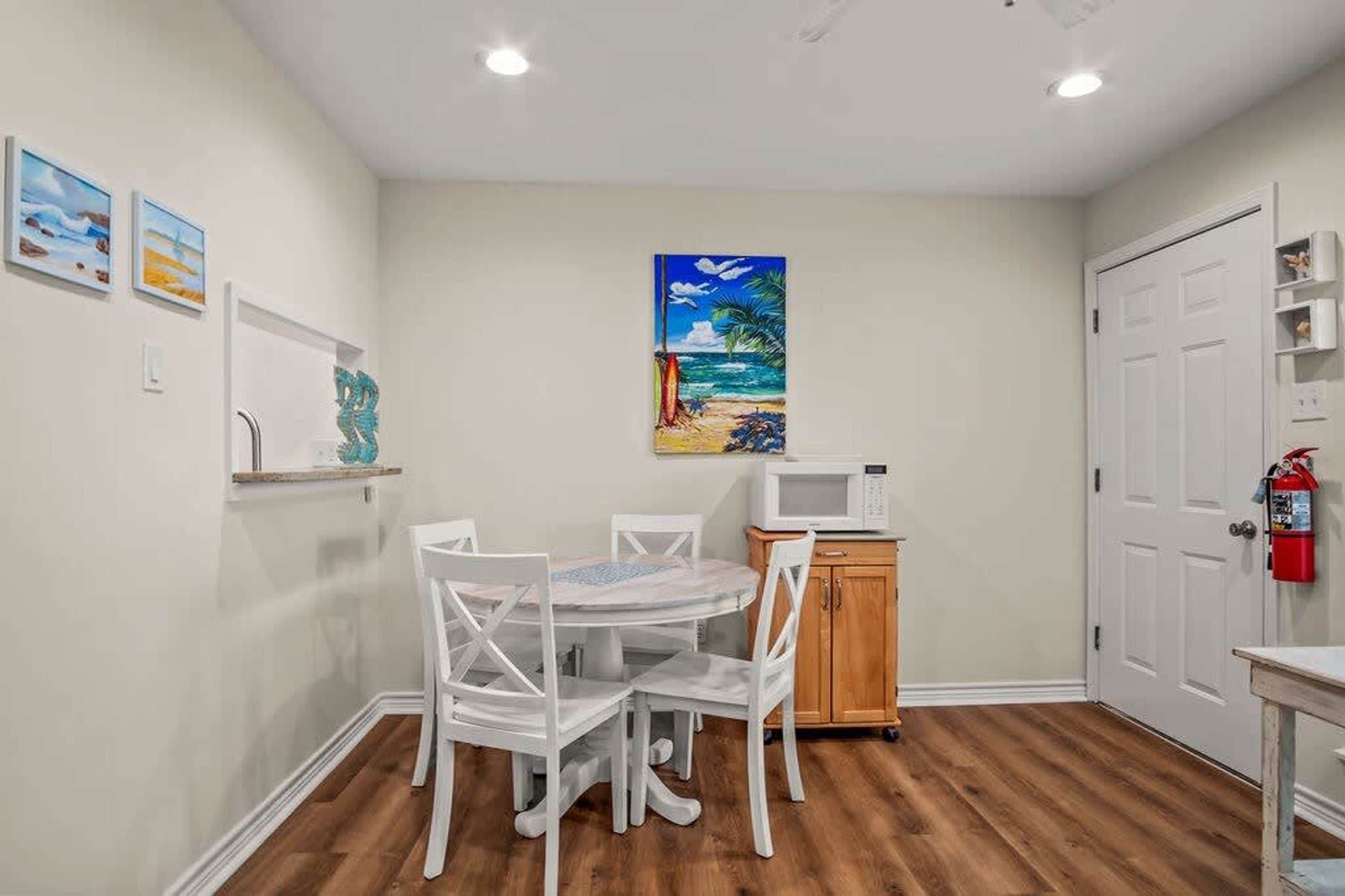A compact kitchen with white cabinetry, a microwave, and a small dining table with chairs.