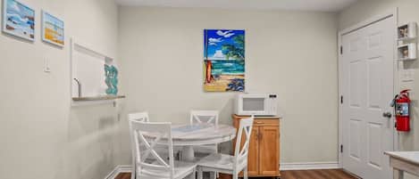 A compact kitchen with white cabinetry, a microwave, and a small dining table with chairs.