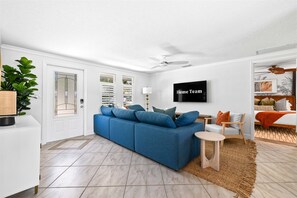 Ein modernes Wohnzimmer mit einem blauen Sofa, einem an der Wand montierten Fernseher und einem Deckenventilator.