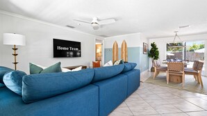 A modern living room with a blue sofa, a ceiling fan, and a flat-screen TV mounted on the wall. - Minutes to Anna Maria Island Pool Mini Golf (Bradenton)