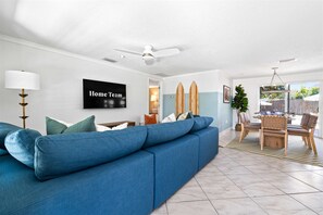 Ein modernes Wohnzimmer mit einem blauen Sofa, einem Deckenventilator und einem wandmontierten Flachbildfernseher.