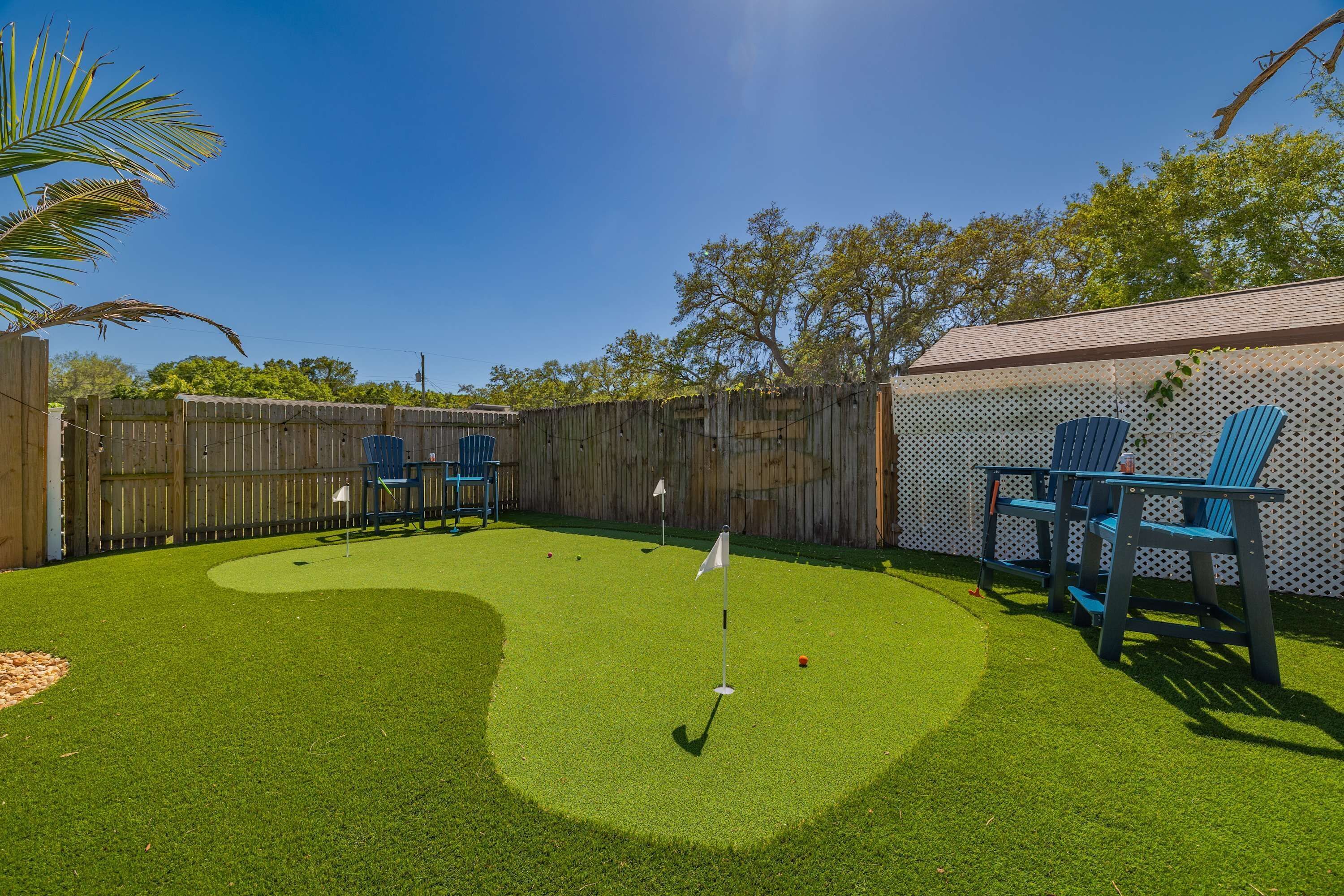 Un patio trasero con césped artificial, un putting green y sillas azules.
