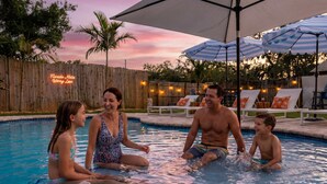A swimming pool with lounge chairs and umbrellas, surrounded by a wooden fence and palm trees. - Minutes to Anna Maria Island Pool Mini Golf (Bradenton)