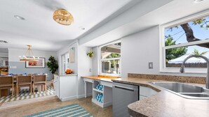 A modern kitchen with a granite countertop, stainless steel sink, and a dining area with a checkered rug. - Minutes to Anna Maria Island Pool Mini Golf (Bradenton)