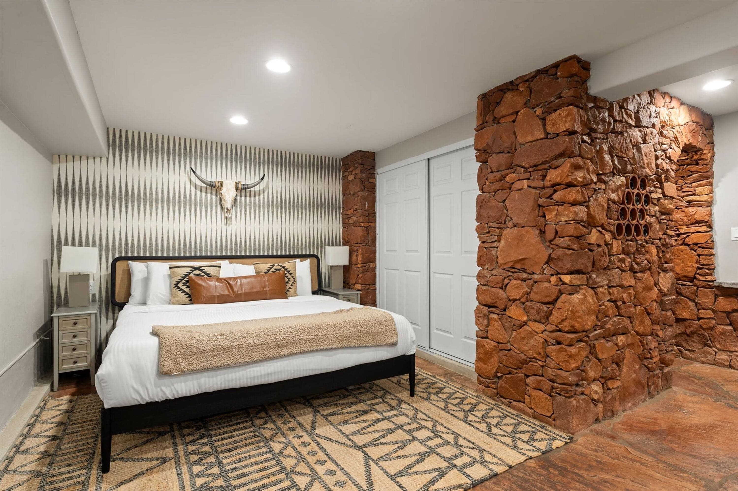 Une chambre moderne avec un mur d’accent en pierre, un lit avec une literie à motifs et une tête de lit décorative.
