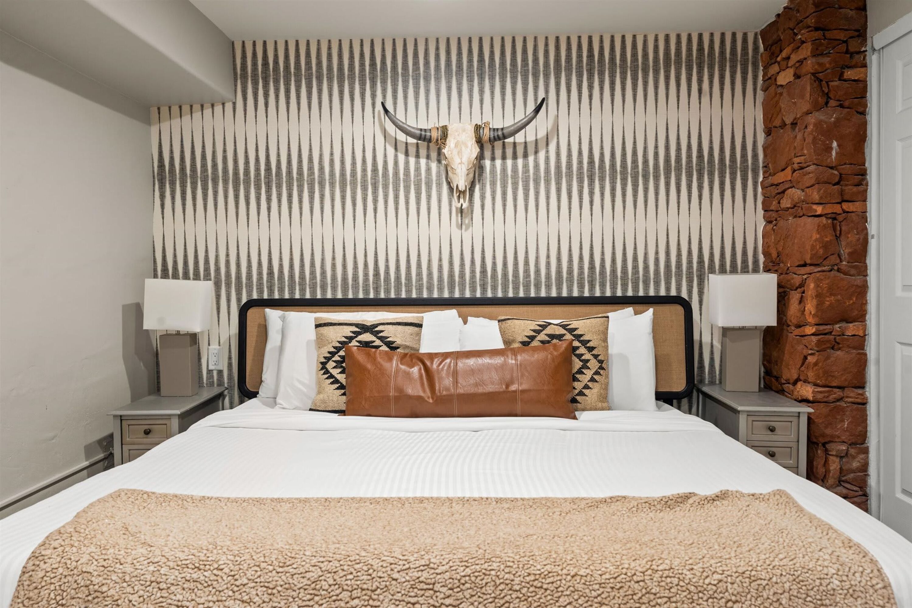 A hotel room with a bed, a stone accent wall, and a decorative skull on the wall.