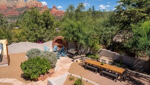 An outdoor patio area with a stone wall, a wooden table, and blue chairs. - The Sedona Sanctuary Hot Tub Unbeatable Views (Sedona)