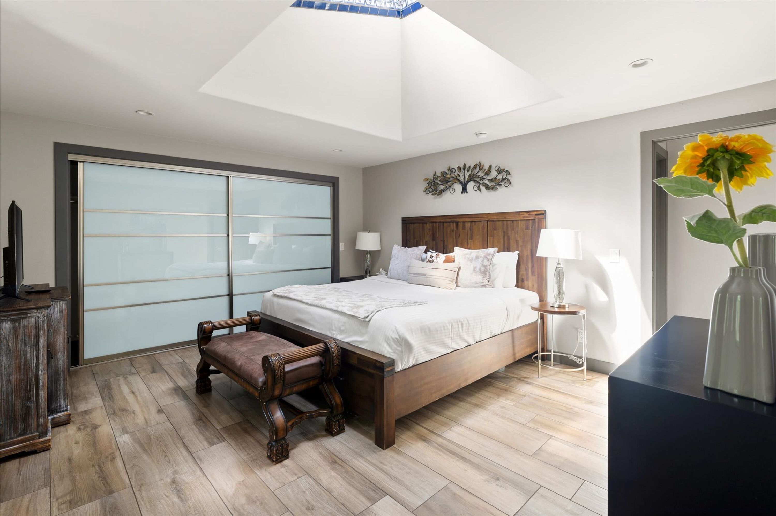A bedroom with a bed, bedside tables, a chair, a desk, and a large window.