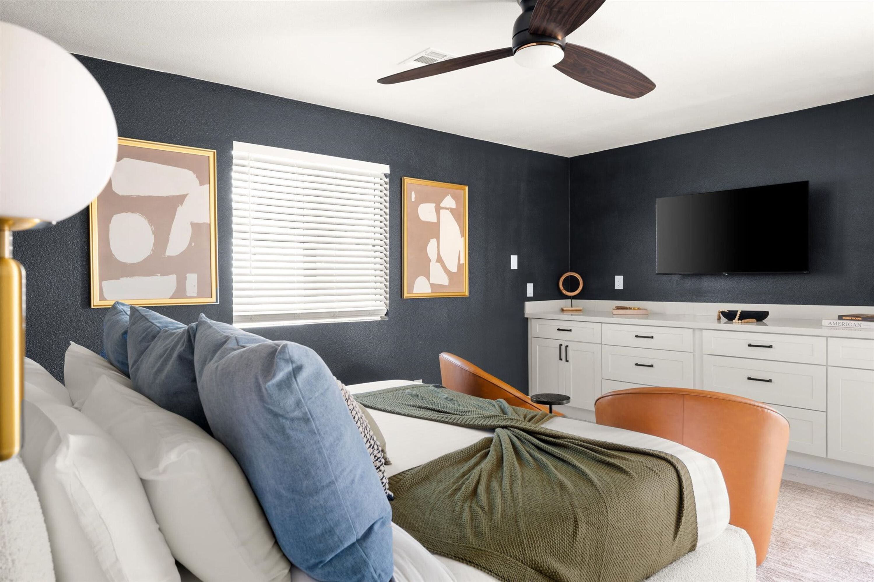 Une chambre à coucher comprenant un lit, un bureau, une chaise, un téléviseur et un ventilateur de plafond.