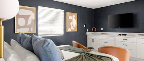 A bedroom with a bed, a desk, a chair, a television, and a ceiling fan.