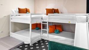 A bunk bed room with white bedding and orange pillows, a patterned rug, and a green chair. - Backyard Pickleball Hottub Pool Gameroom (Phoenix)