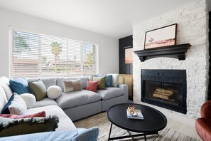 A modern living room with a grey sofa, a fireplace, and a round black coffee table. - Backyard Pickleball Hottub Pool Gameroom (Phoenix)