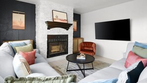 A modern living room with a white sofa, a fireplace, a television mounted on the wall, and a red armchair. - Backyard Pickleball Hottub Pool Gameroom (Phoenix)
