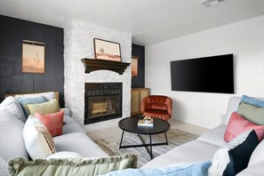 Ein modernes Wohnzimmer mit einem weißen Sofa, einem Kamin, einem an der Wand befestigten Fernseher und einem roten Sessel.