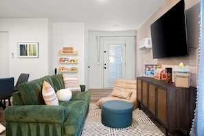Un salon avec un canapé vert, un pouf bleu, un téléviseur et un meuble contenant des jouets.