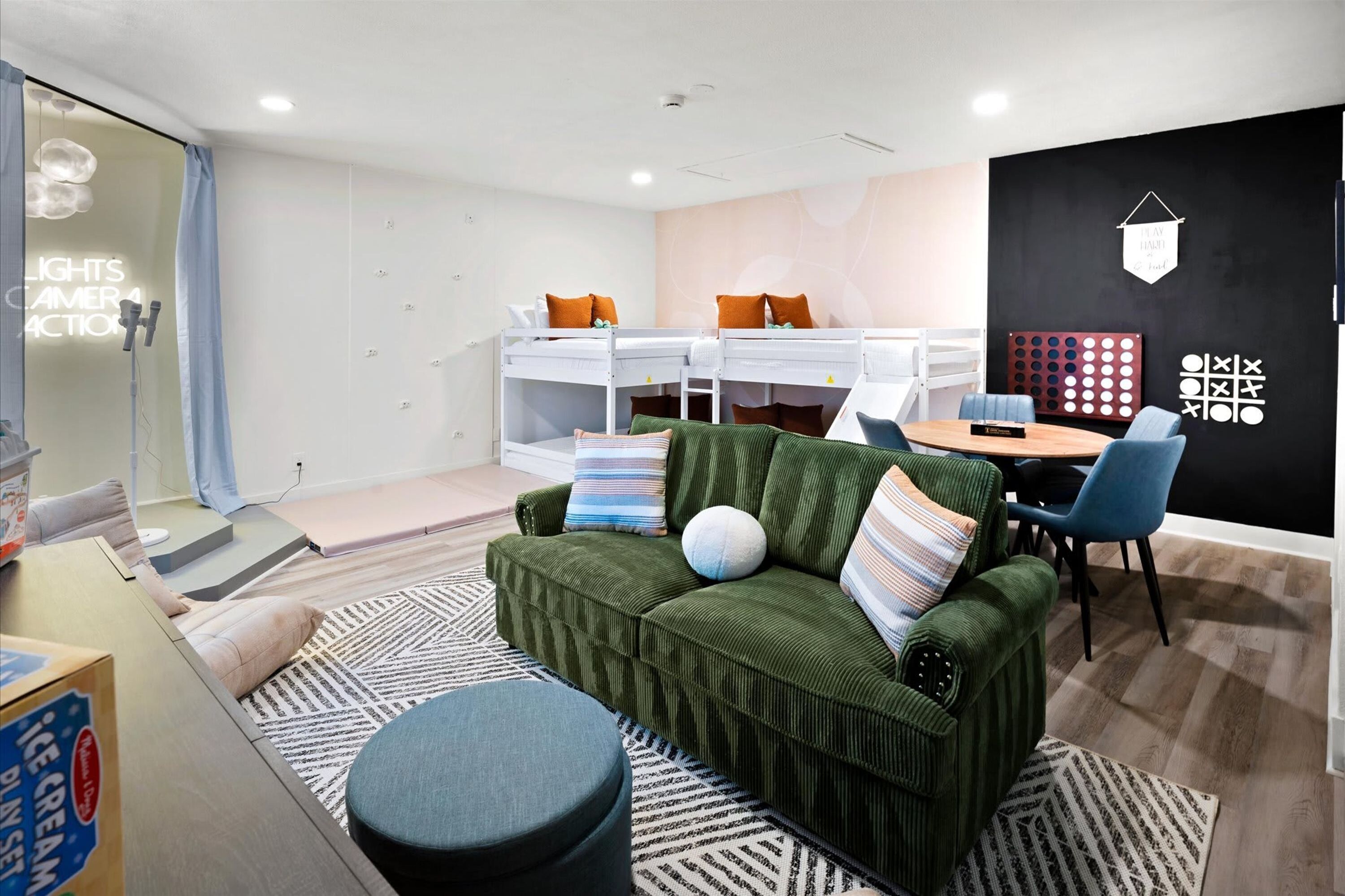 A modern room with a bunk bed, a green sofa, a round ottoman, and a dining area with a table and chairs.