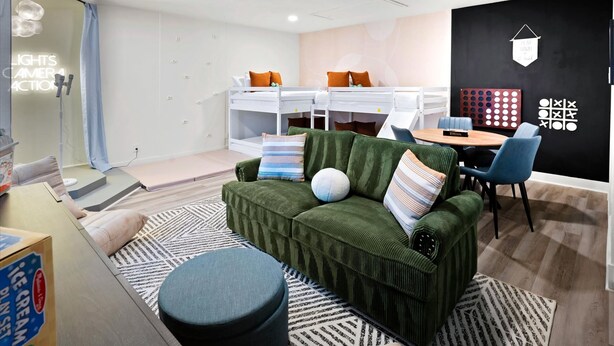 A modern room with a bunk bed, a green sofa, a round ottoman, and a dining area with a table and chairs. - Backyard Pickleball Hottub Pool Gameroom (Phoenix)