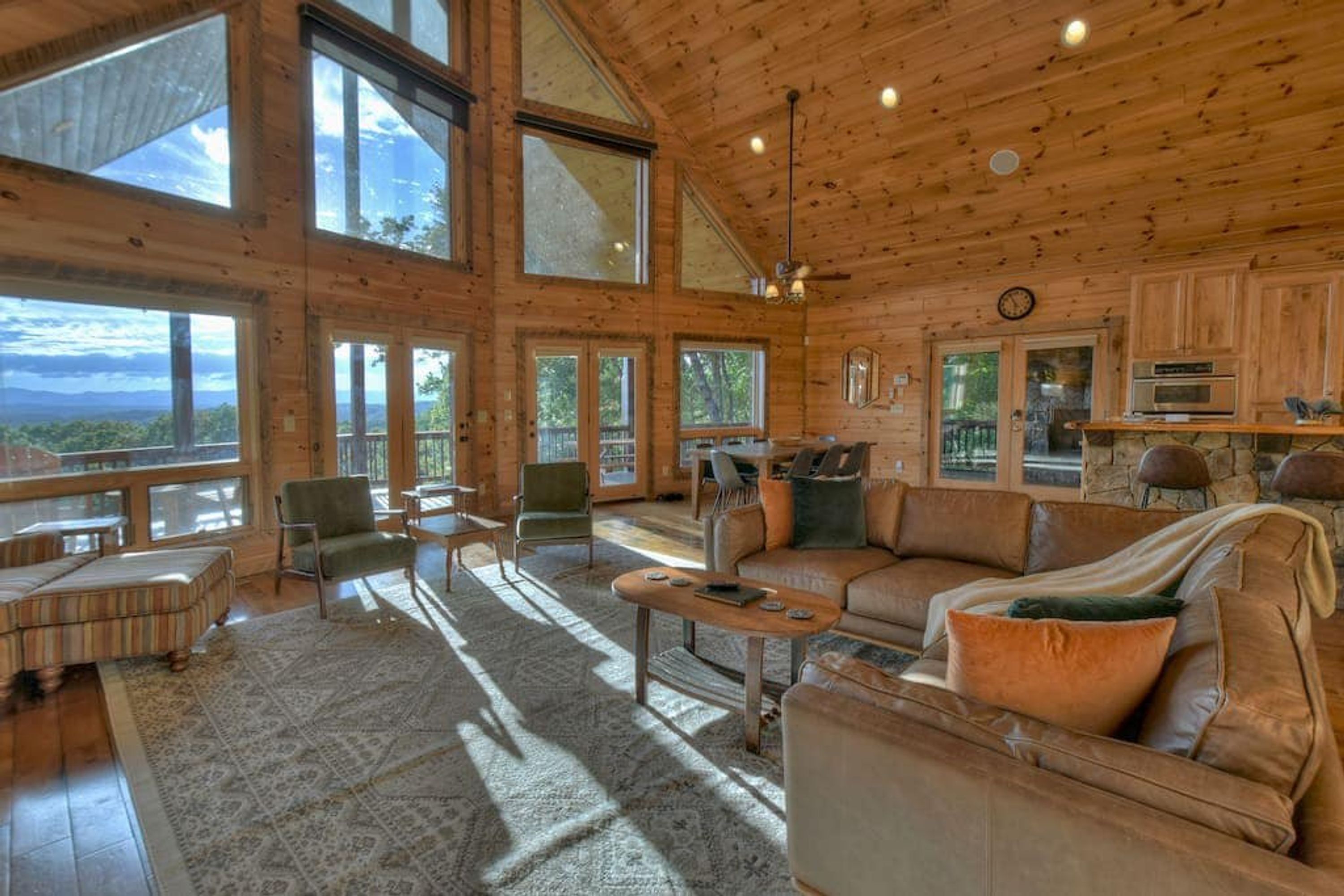 A spacious wooden cabin with large windows, a cozy seating area, and a stone fireplace.
