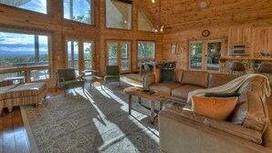 A spacious wooden cabin with large windows, a cozy seating area, and a stone fireplace. - Endless Views Hot Tub Movie Theater Firepit (Mineral Bluff)