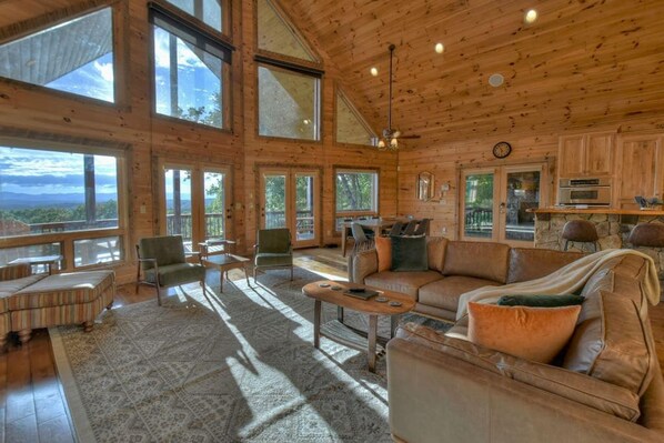 A spacious wooden cabin with large windows, a cozy seating area, and a stone fireplace.