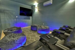 A home theater room with a flat-screen TV mounted on the wall, two bean bag chairs, and a row of leather recliner sofas.