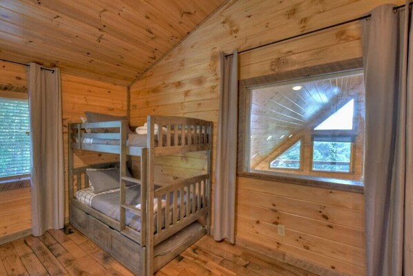 A wooden cabin interior with a bunk bed, a window with a view, and curtains. - Endless Views Hot Tub Movie Theater Firepit (Mineral Bluff)