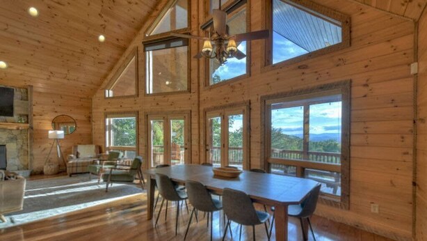 A spacious room with a large dining table and chairs, a fireplace, and large windows offering views of the outdoors. - Endless Views Hot Tub Movie Theater Firepit (Mineral Bluff)