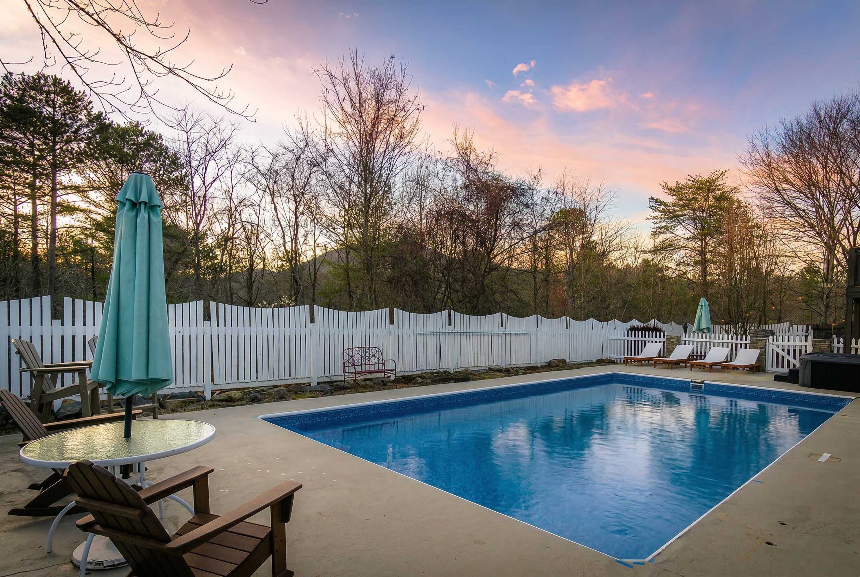 Ein rechteckiger Pool mit weißer Liegefläche, umgeben von einem weißen Zaun, mit Sonnenuntergang im Hintergrund.