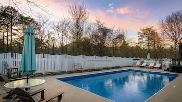 Ein rechteckiger Pool mit weißer Liegefläche, umgeben von einem weißen Zaun, mit Sonnenuntergang im Hintergrund.